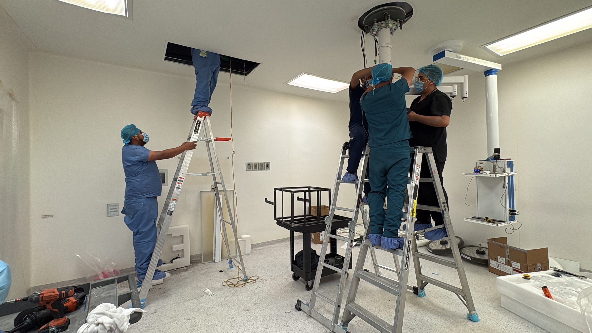 Equipo de BioMed Innovate instalando lámparas de cirugía en un quirófano, con dos escaleras y brazos de techo montados